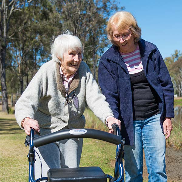 elderly woman walking outside assisted by a female volunteer