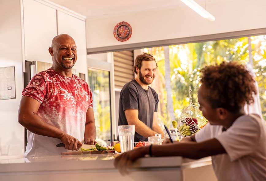 two men smiling and cooking for a child in their home